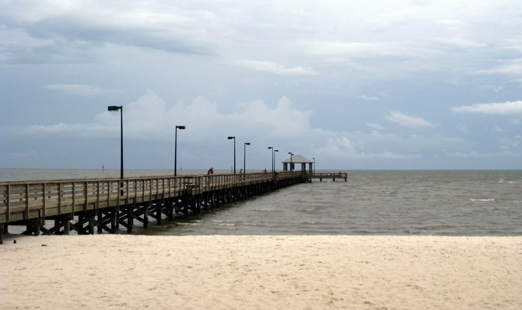 A long wooden pier goes out onto the ocean water along a beach