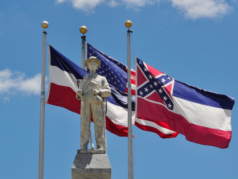 Three flags fly near a monument to a soldier