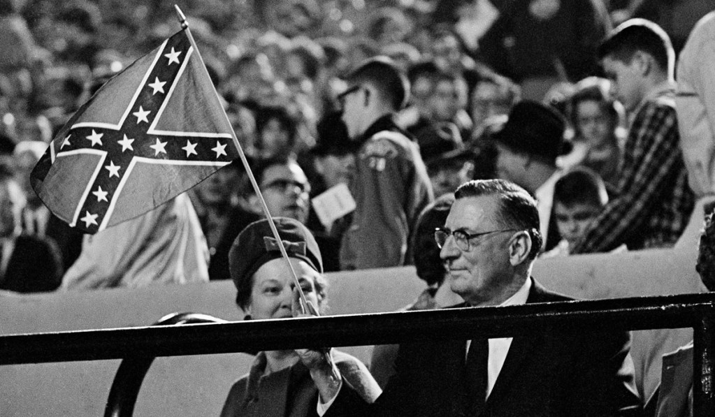An old 1960's black and white photo showing Gov. Ross Barnett, seated at a football game and waving a small Confederate flag