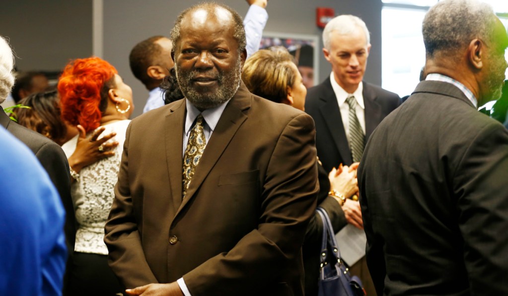 Robert Walker, in a brown suit, stands in a crowded room