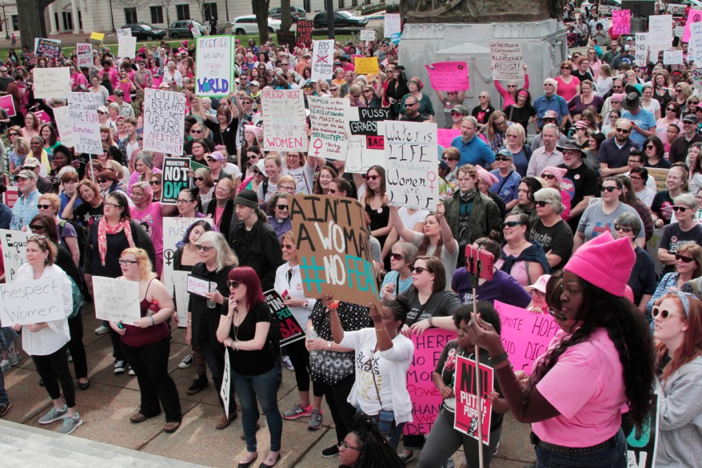 Dozens of people, including numerous women, holding signs at a women’s rights march.