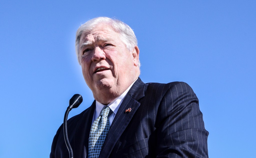 an older man with white hair and wearing a suit speaks at a microphone