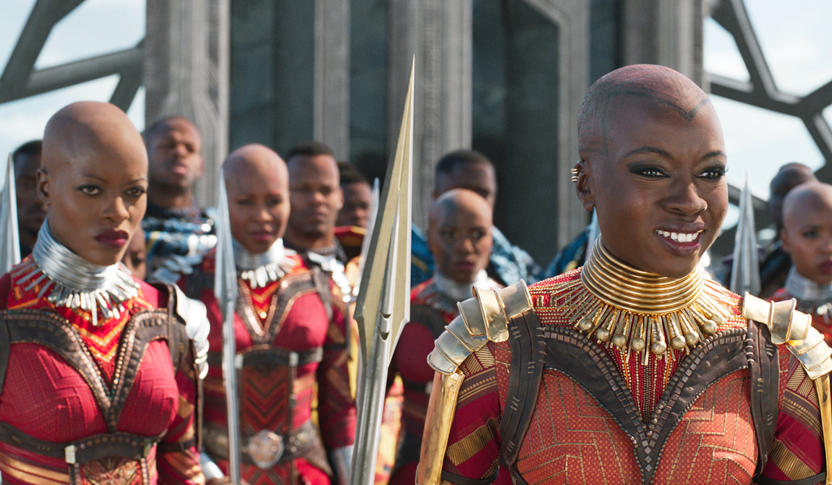 A still from a movie depicting many bald women with red outfis and metal worked details, with matching metal spears