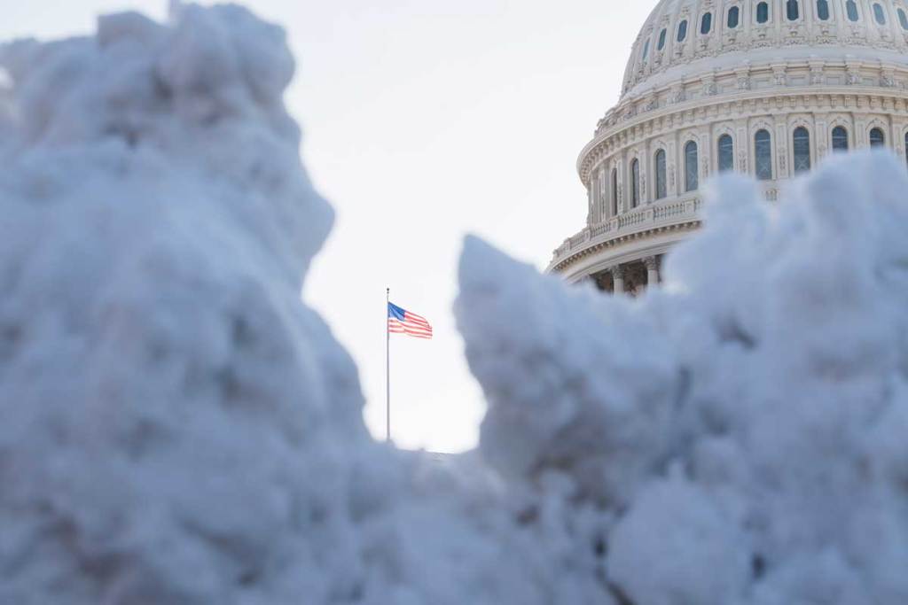 A photo of the U.S. flag between two snow banks. The U.S. Capitol building is in the background.