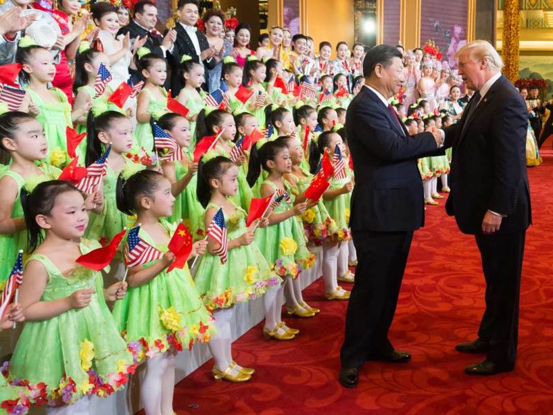 Donald Trump shakes hands with Xi Jinping in front of rows of children dressed for a performance and holding US and China flags