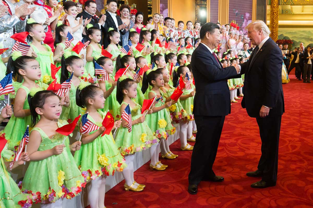 Donald Trump shakes hands with Xi Jinping in front of rows of children dressed for a performance and holding US and China flags