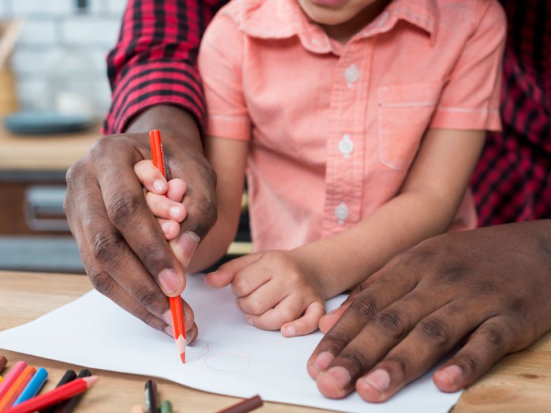 Closeup of a father helping a small child use color pencils on paper