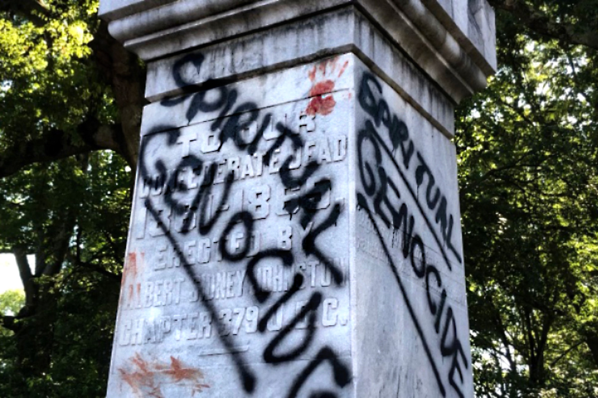 Defaced confederate statue that says Spiritual Genocide in spraypaint across the faces
