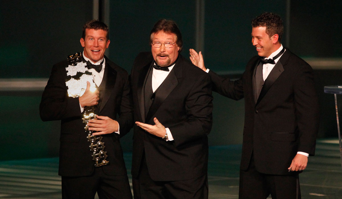 Ted DiBiase Sr., Brett DiBiase, and Ted DiBiase Jr. stand on a stage smiling together