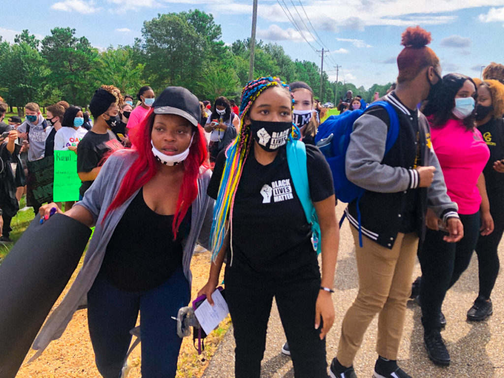 a photo showing Black teens wearing Black Lives Matter masks with a multiracial group of students behind them protesting outside