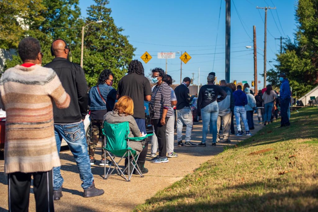 A long line of people stand on a sidewalk to vote