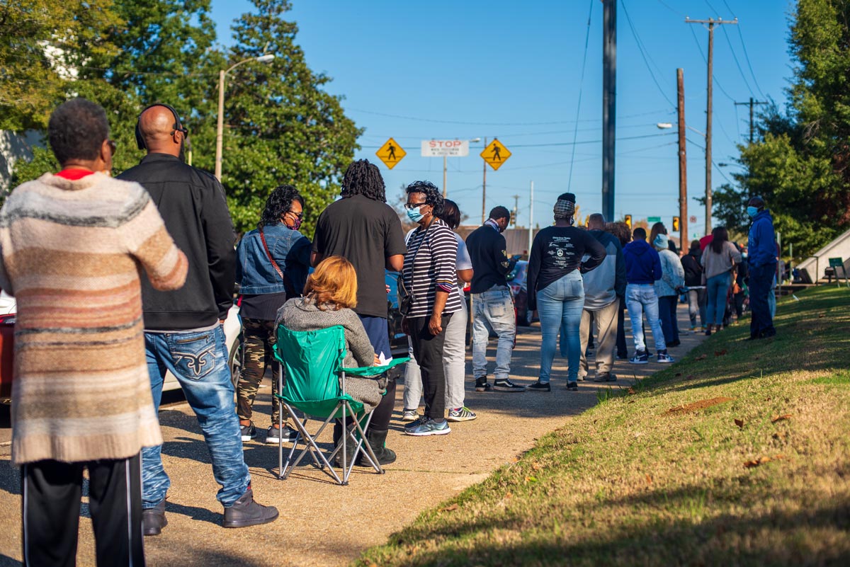 A long line of people stand on a sidewalk to vote