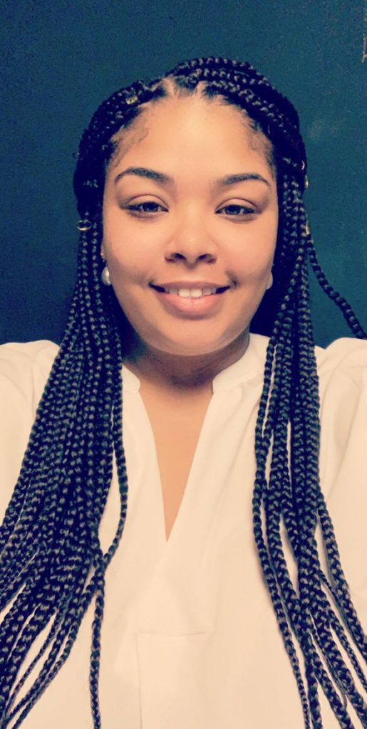 Headshot of DeLia Kennedy smiling with box braids and pearl earrings