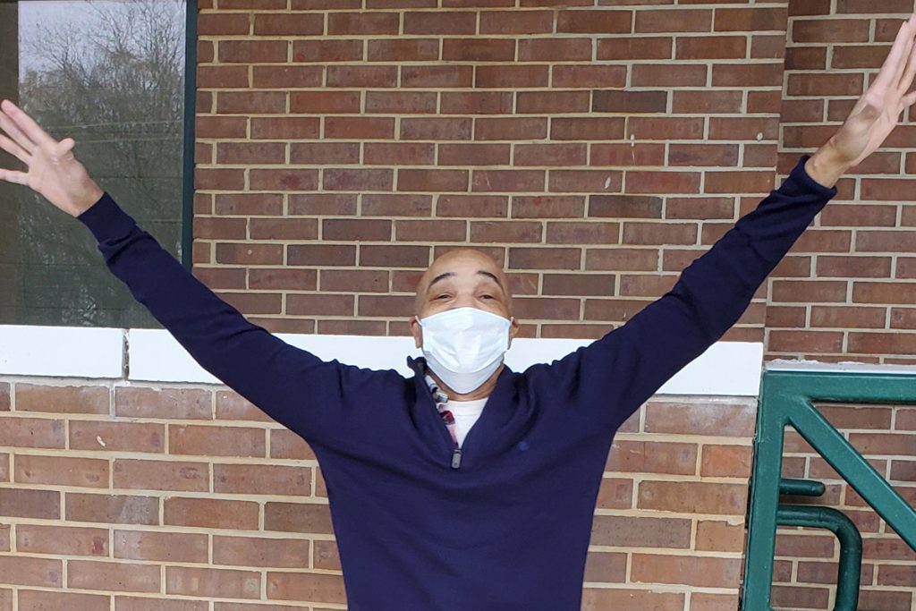 Eddie Lee Howard wearing a blue long sleeve shirt and medical mask with arms raised out