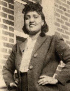 Old photo of a smiling woman in front of a brick wall