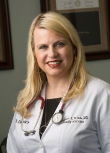 Dr Jennifer Bryan looking at the camera. She has long blonde hair, a red stethoscope around her neck and a white lab coat on