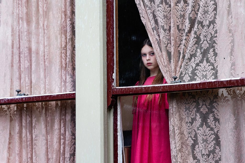 Girl in pink dress looking through pink curtains