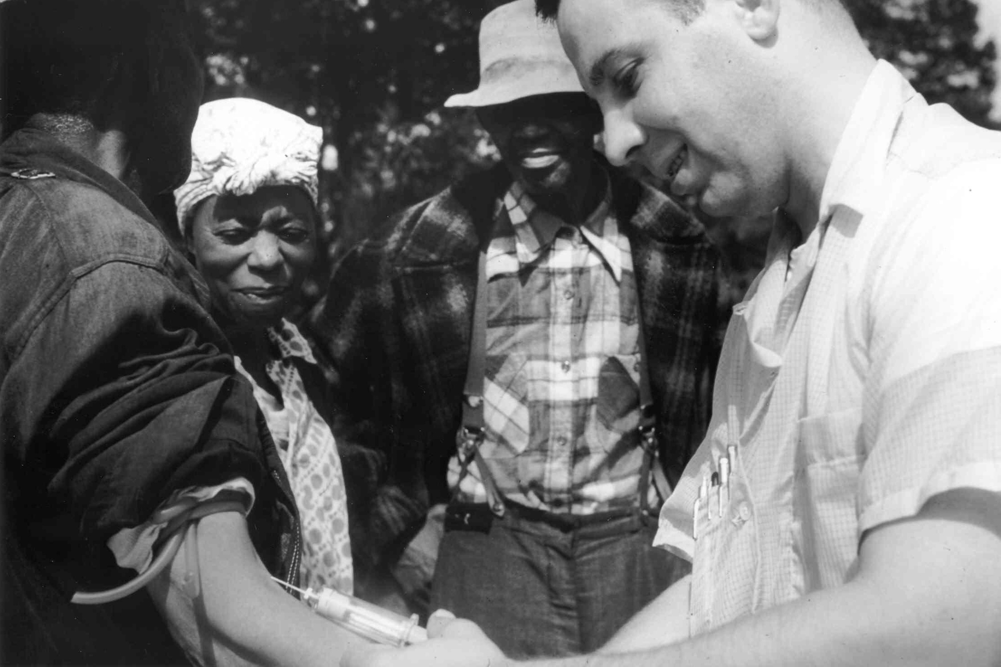White man injecting a black man while two others watch