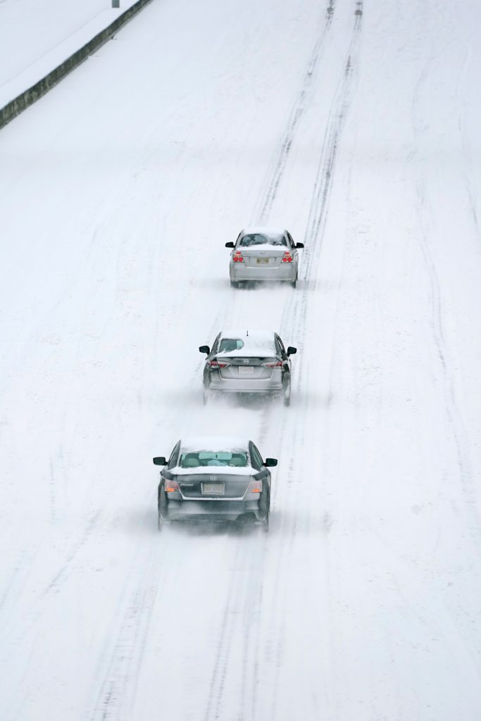 Three snow-covered cars driving in single file down an icy interstate