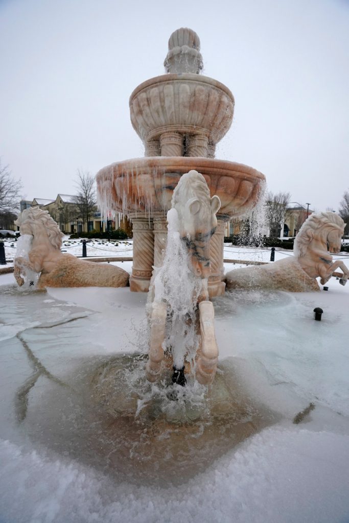 A large fountain with marble horses, filled with frozen water