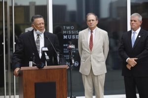Reuben Anderson speaks at a podium outside the Two Mississippi Museums as Lieutenant Governor Delbert Hosemann and Mississippi House Speaker Philip Gunn look on.