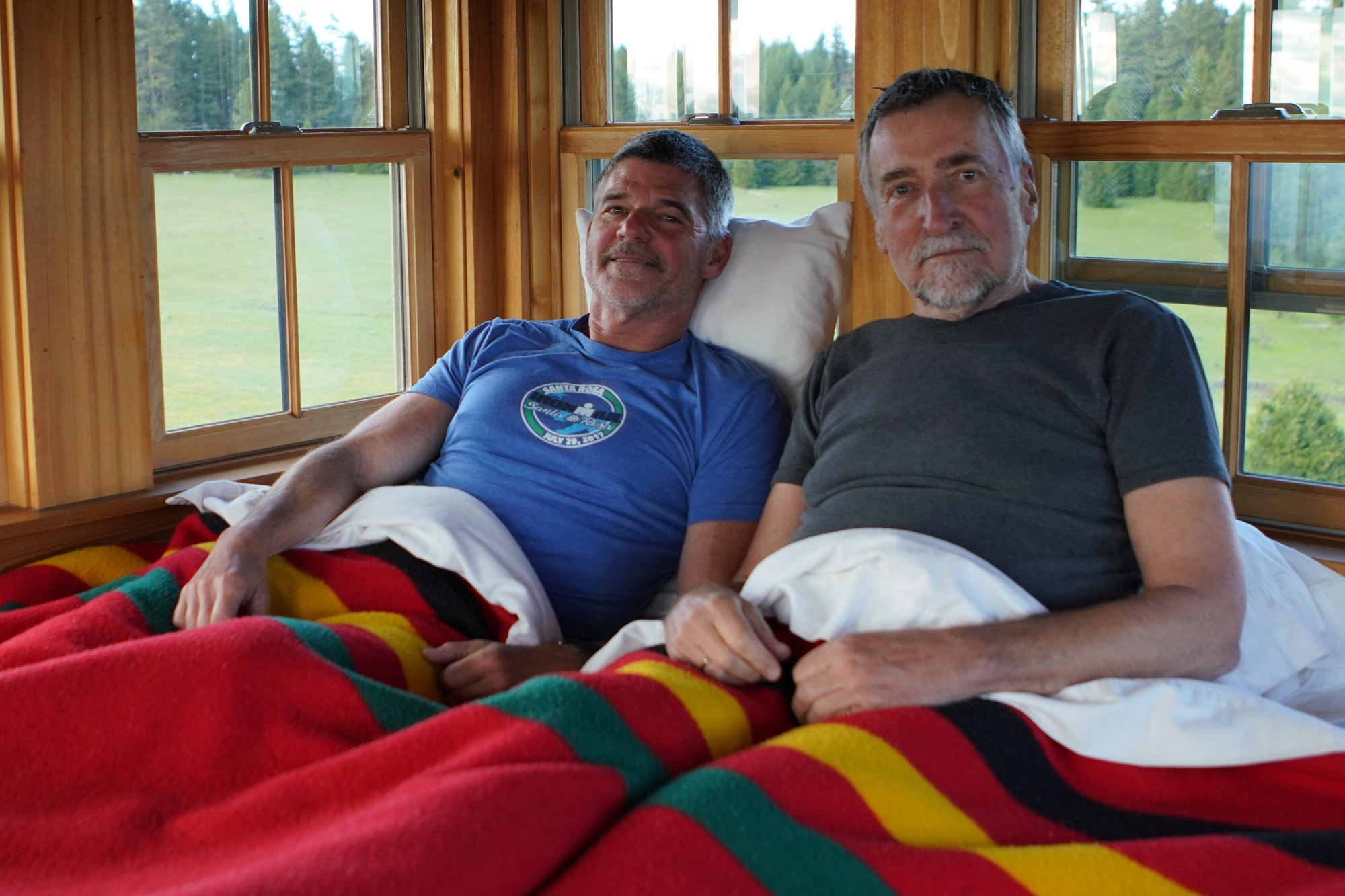 Two men in bed under a bright red blanket