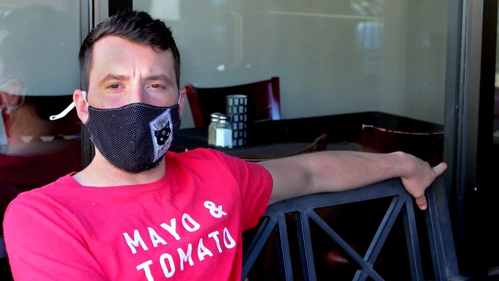 Chef Eric Tate sits wearing a Black mask and a red T-shirt reading Mayo & Tomato.