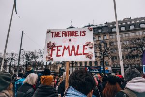 White poster with red writing held up saying the future is female in crowd of women protest