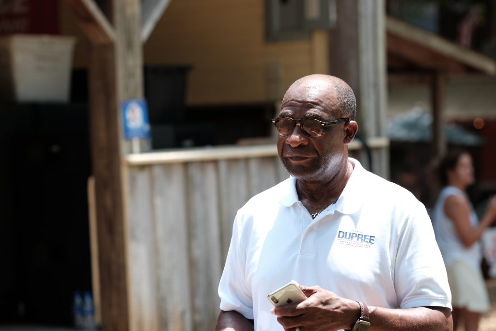 Mayor Johnny DuPree, a Black man, walking at the Neshoba County Fair wearing a white campaign polo shirt with his last name over the pocket
