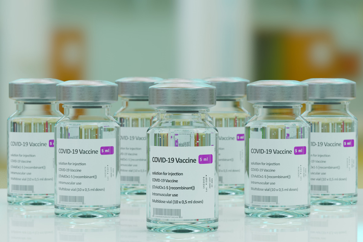 Eight 5mL vials of COVID-19 vaccine arranged on a white surface.