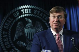 Governor Tate Reeves stands in front of the seal of Mississippi speaking