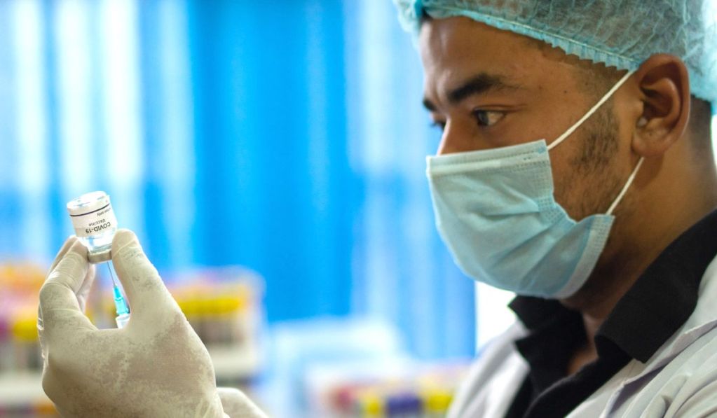 A masked physician draws a vaccine from a vial