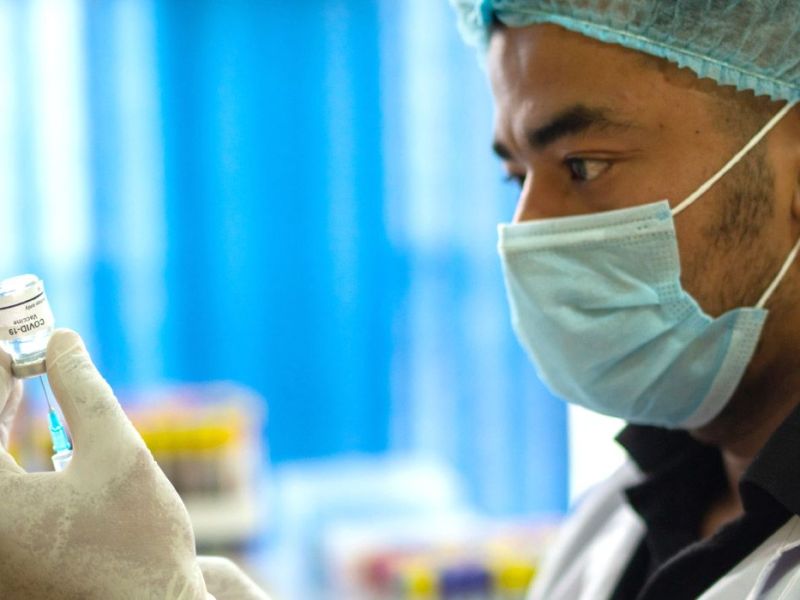 A masked physician draws a vaccine from a vial