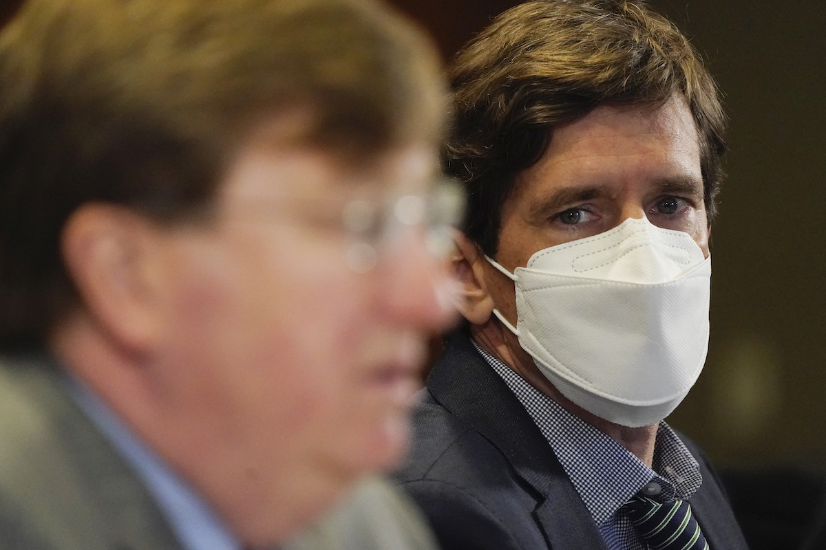 Dr. Dobbs, wearing a mask, looks at Governor Tate Reeves as Reeves speaks in a press conference.