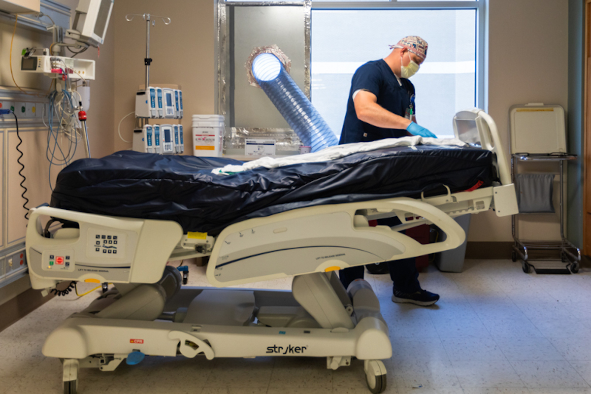 A male healthcare professional prepares a hospital room for a COVID-19 patient.