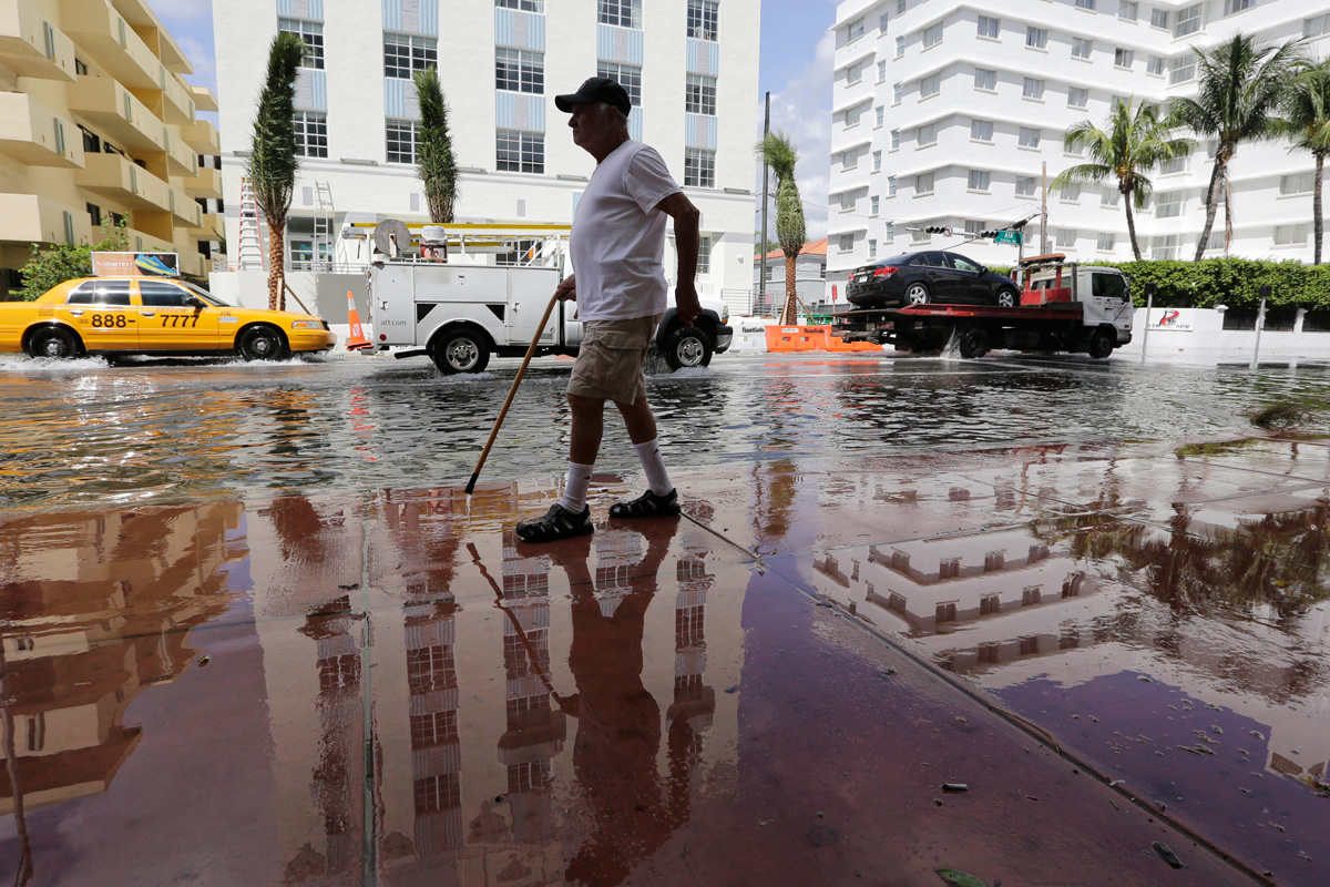 Flooded Miami strees with an elderly man walking with a cane in the foreground