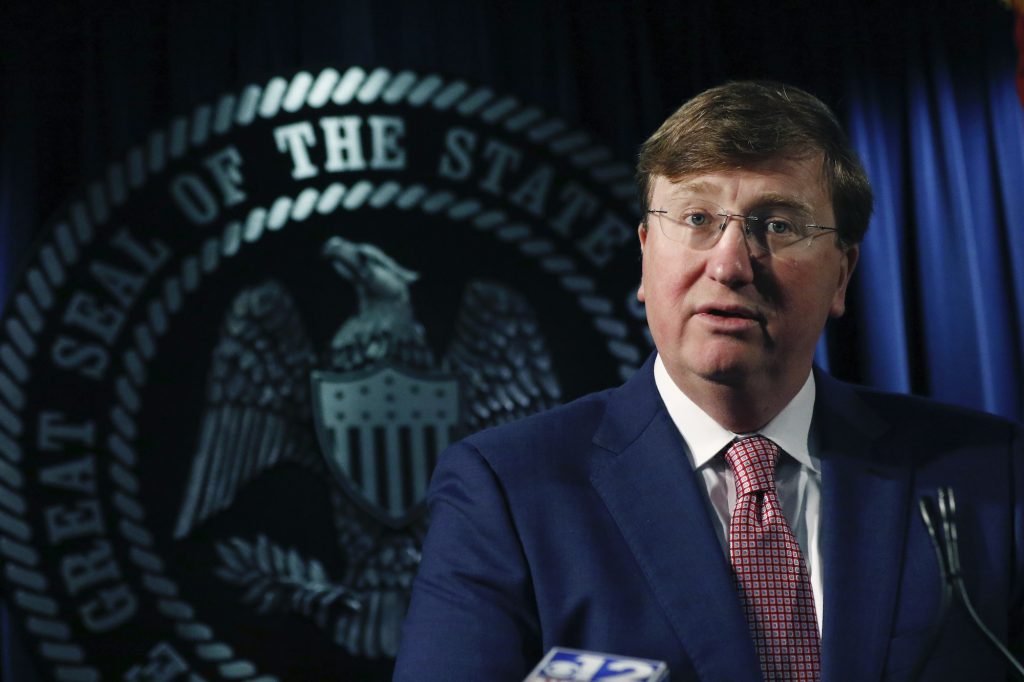 Gov Tate Reeves stands in front of the state seal speaking to reporters