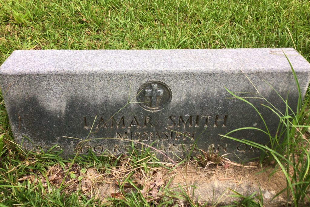 Grass blades around a short, rectangular tombstone for Lamar Smith, a World War I veteran and lynching victim in Brookhaven, Mississippi, in 1955
