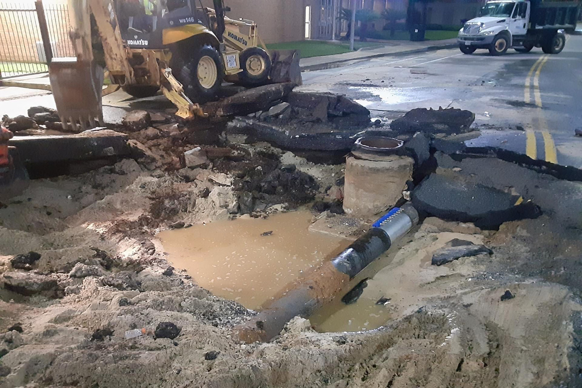 A ruptured water main on Main Street. The pipe is dug up and surrounded by muddy water.