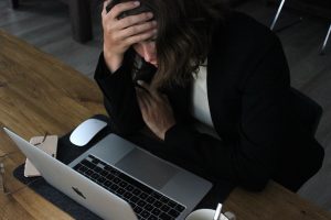 Stressed woman holding her head while bent over a laptop