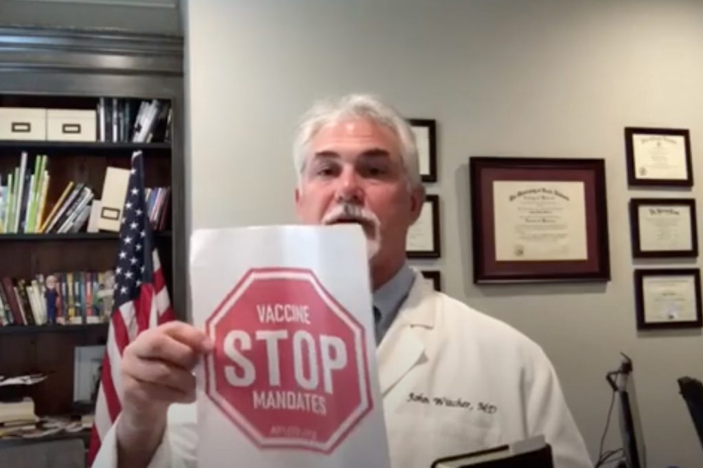 Dr John Witcher holds up a piece of paper with a red stop sign saying 'Stop Vaccine Mandates'