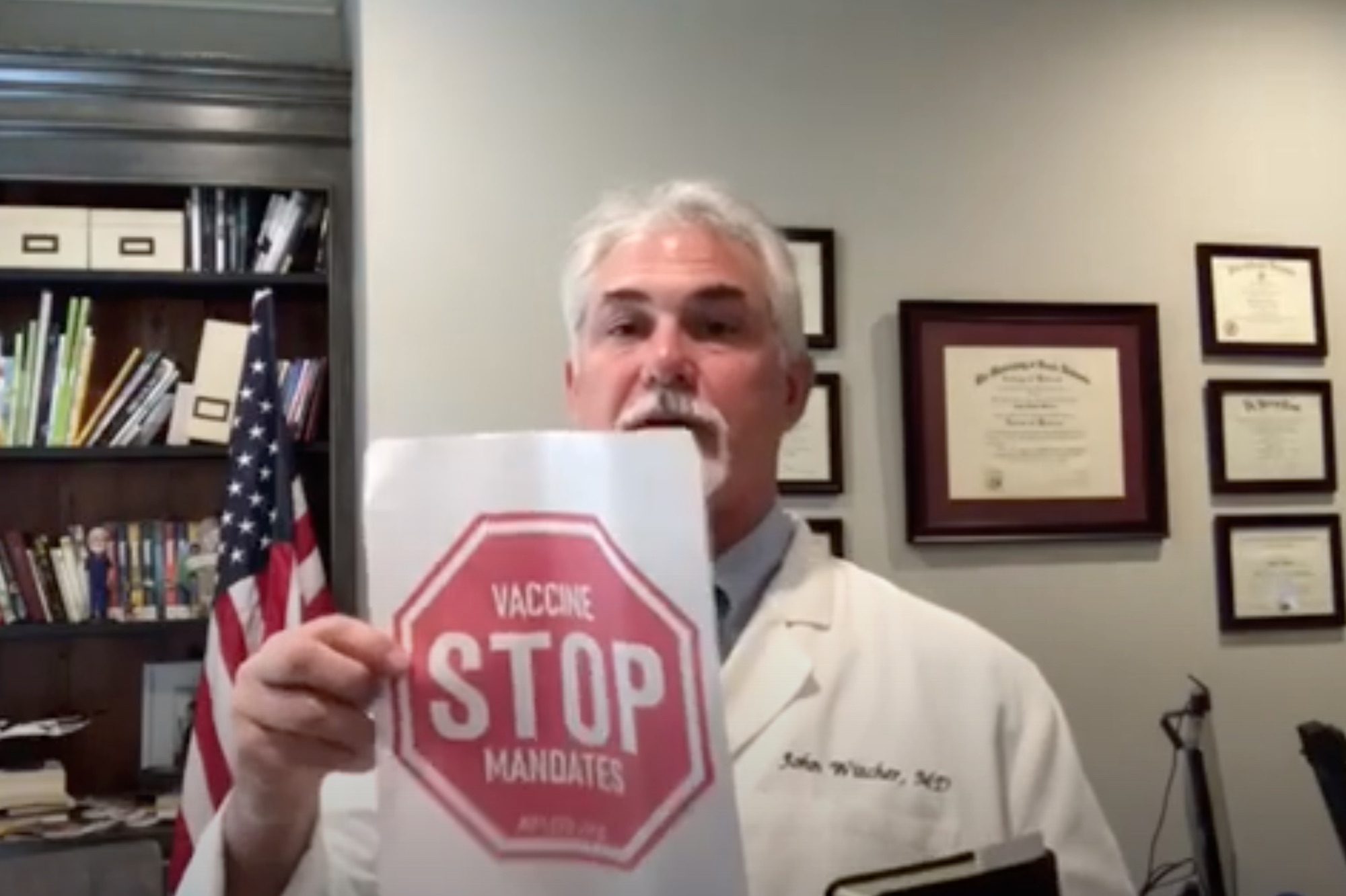 Dr John Witcher holds up a piece of paper with a red stop sign saying 'Stop Vaccine Mandates'