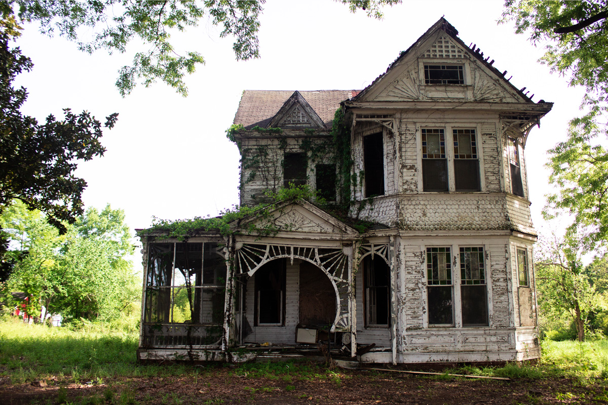 An old white victorian home with vines growing across it and signs of neglect