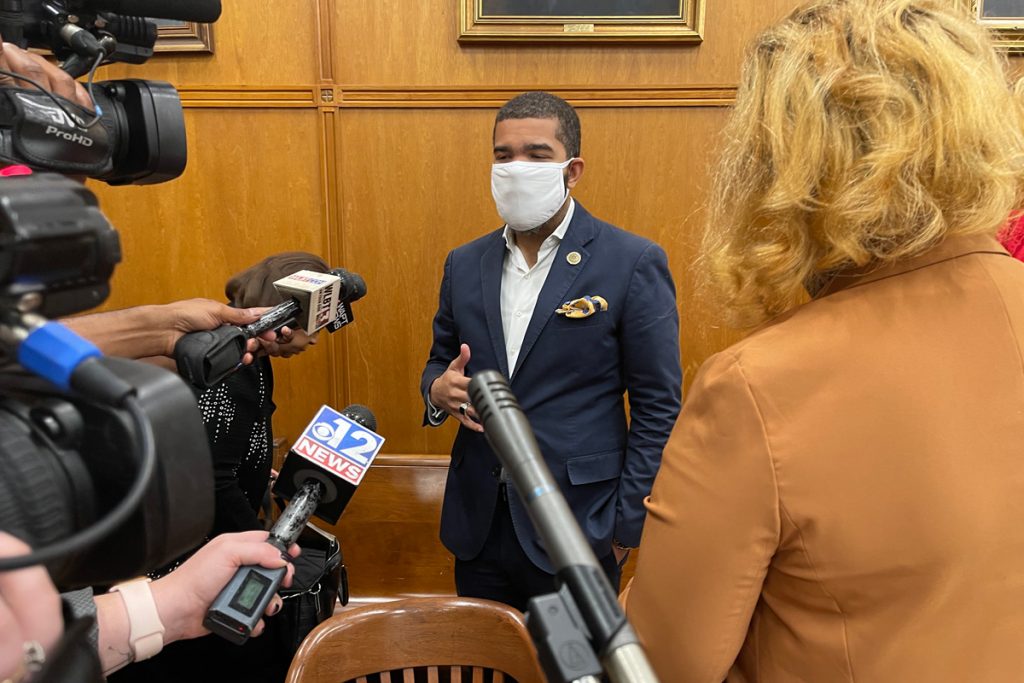 Mayor Chokwe A. Lumumba in a mask, blue suit and no tie, addressing a wall of reporters