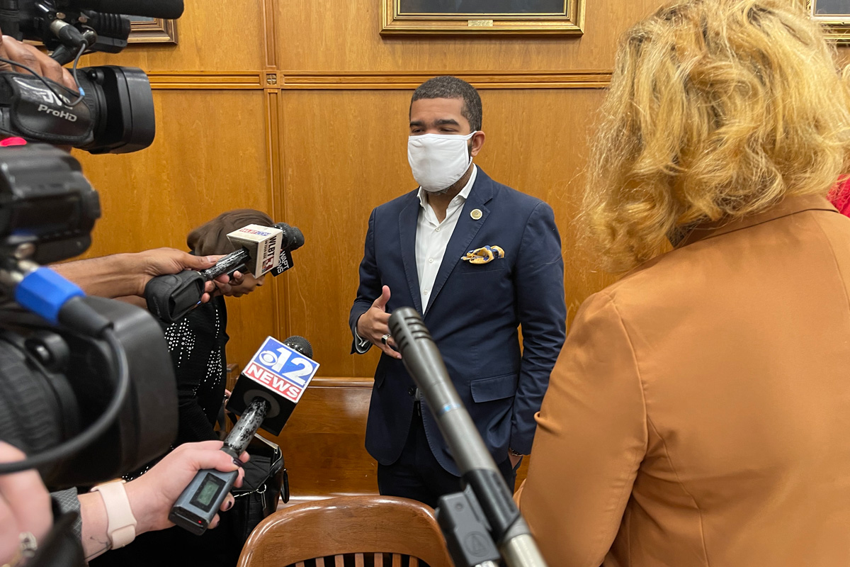 Mayor Chokwe A. Lumumba in a mask, blue suit and no tie, addressing a wall of reporters