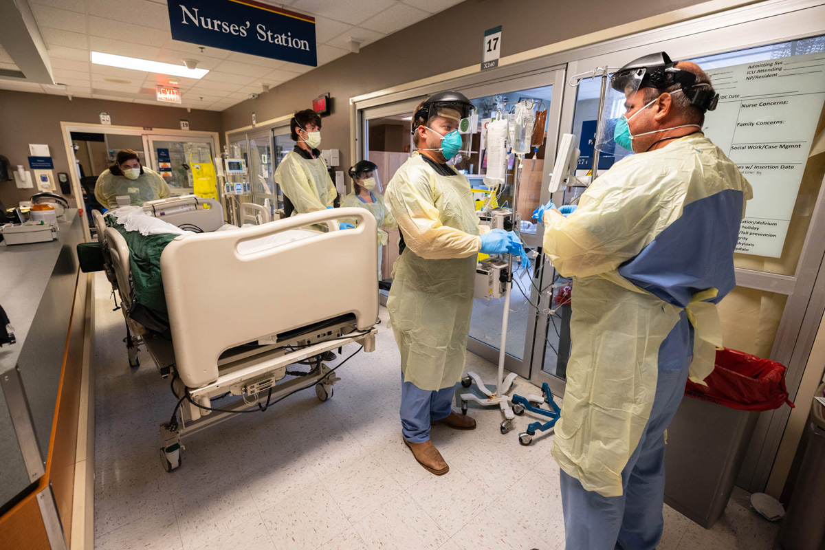 Nurse's Station with four medical professionals dressed in PPE, preparing a rolling bed for a COVID patient