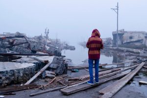 Person in a hooded jacket overlooking a wrecked city block