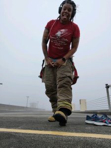 Lavonda Aldrich, wearing firefighter pants and a red graphic tshirt, posing in front of the camera on a foggy day