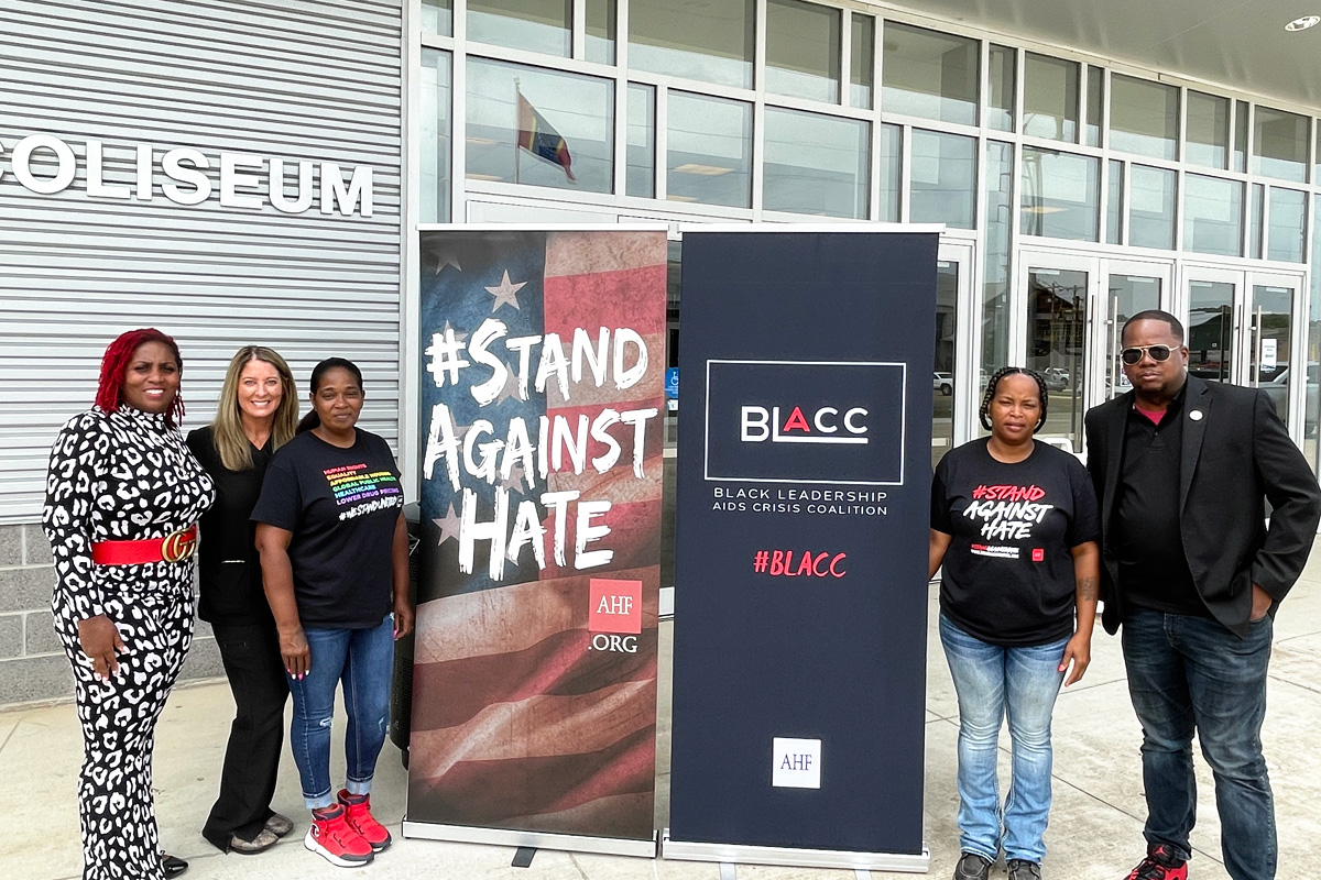 Five people standing beside signs that say Stand Against Hate and BLACC