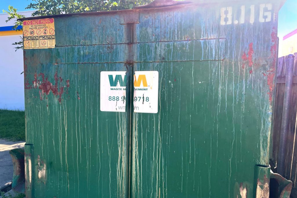 Close up of the side of a green garbage bin with a Waste Management label
